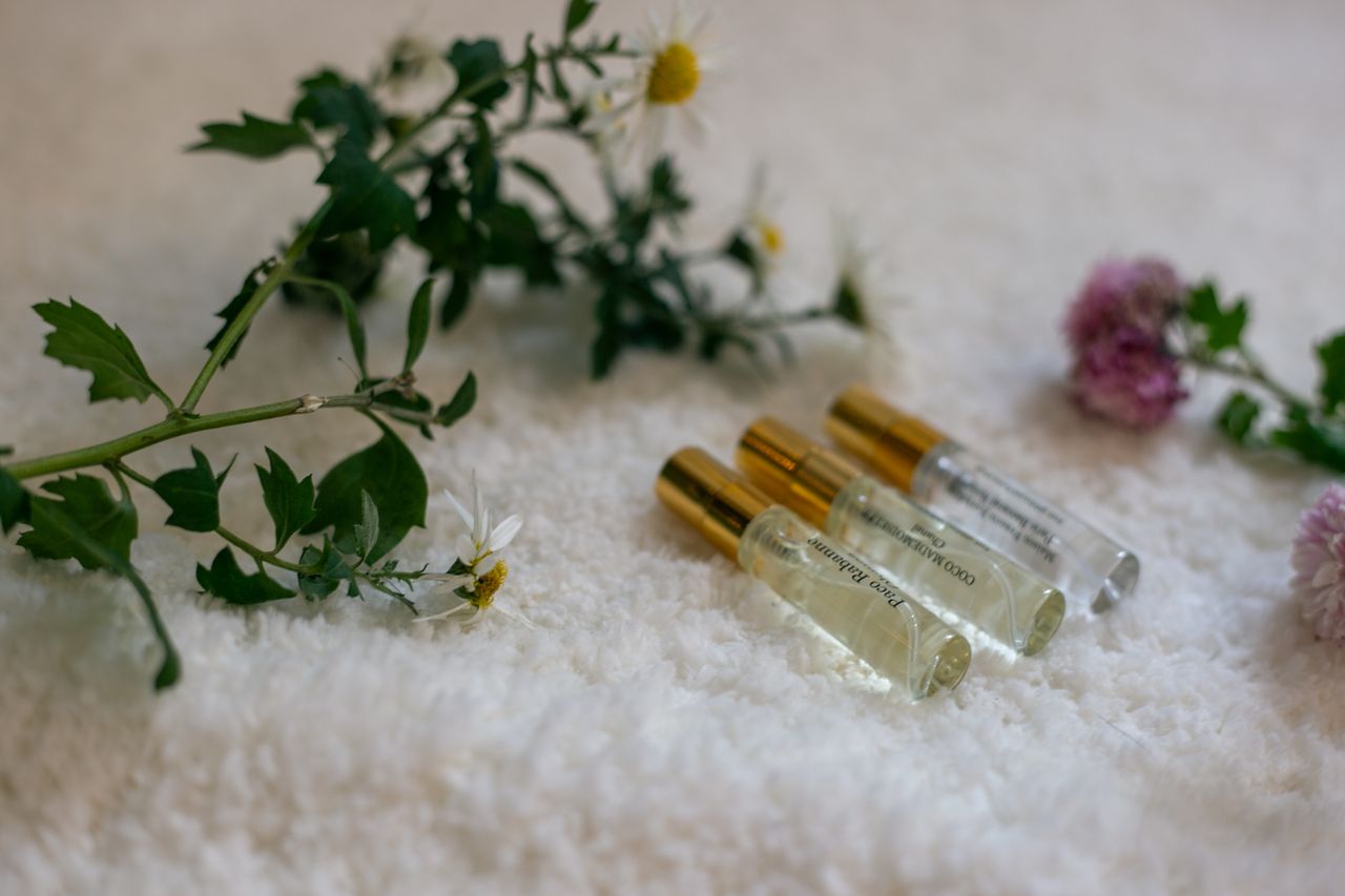 Three glass perfume bottles beside delicate flowers on a white surface.